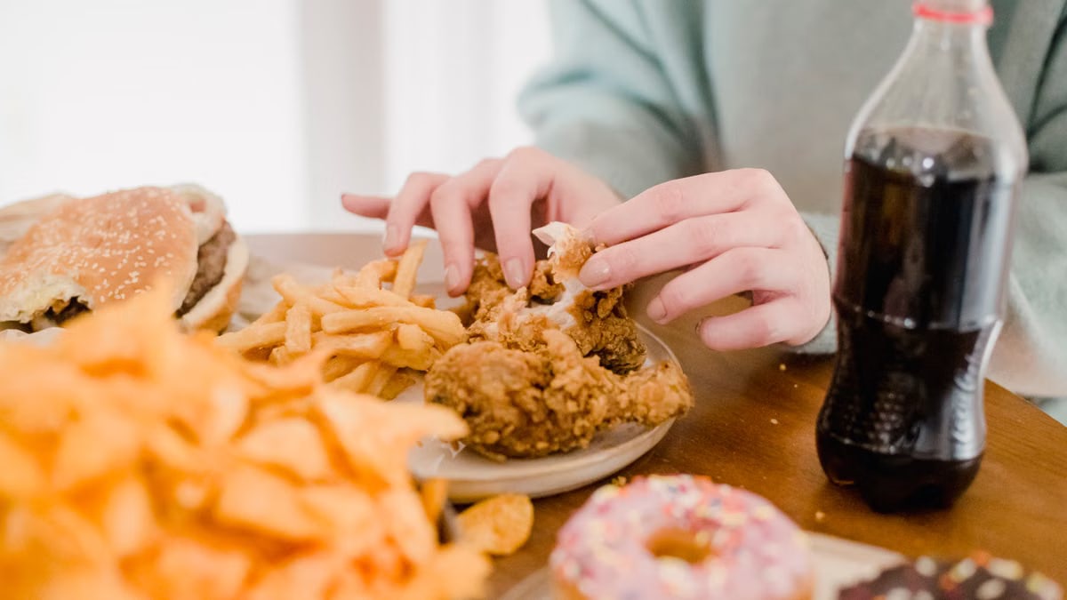 Crop anonymous female eating appetizing spicy fried chicked at table with different snacks